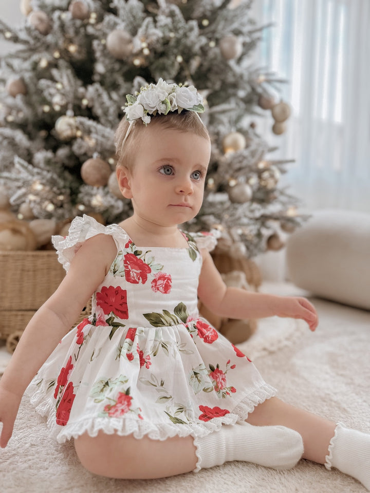 Baby girl wearing Faith Floral Christmas Romper with red and green florals sitting by the Christmas tree
