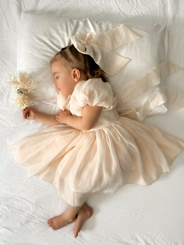 Baby wearing Lucy Champagne Dress with puff sleeves and bow on the back
