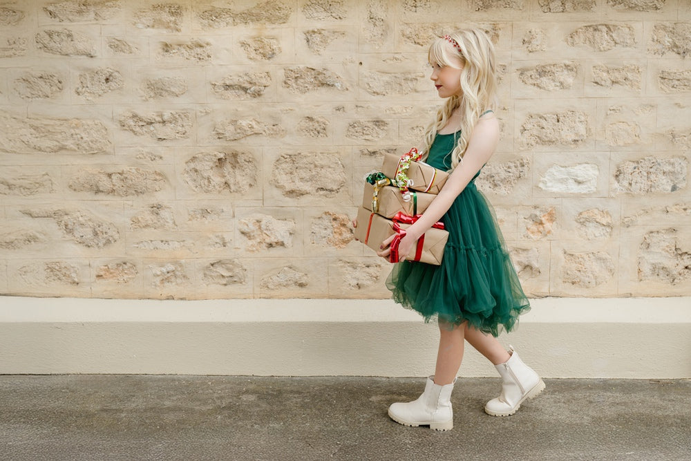A girl in a red Christmas dress holding a gold star, she has a gold tiara in her hair.