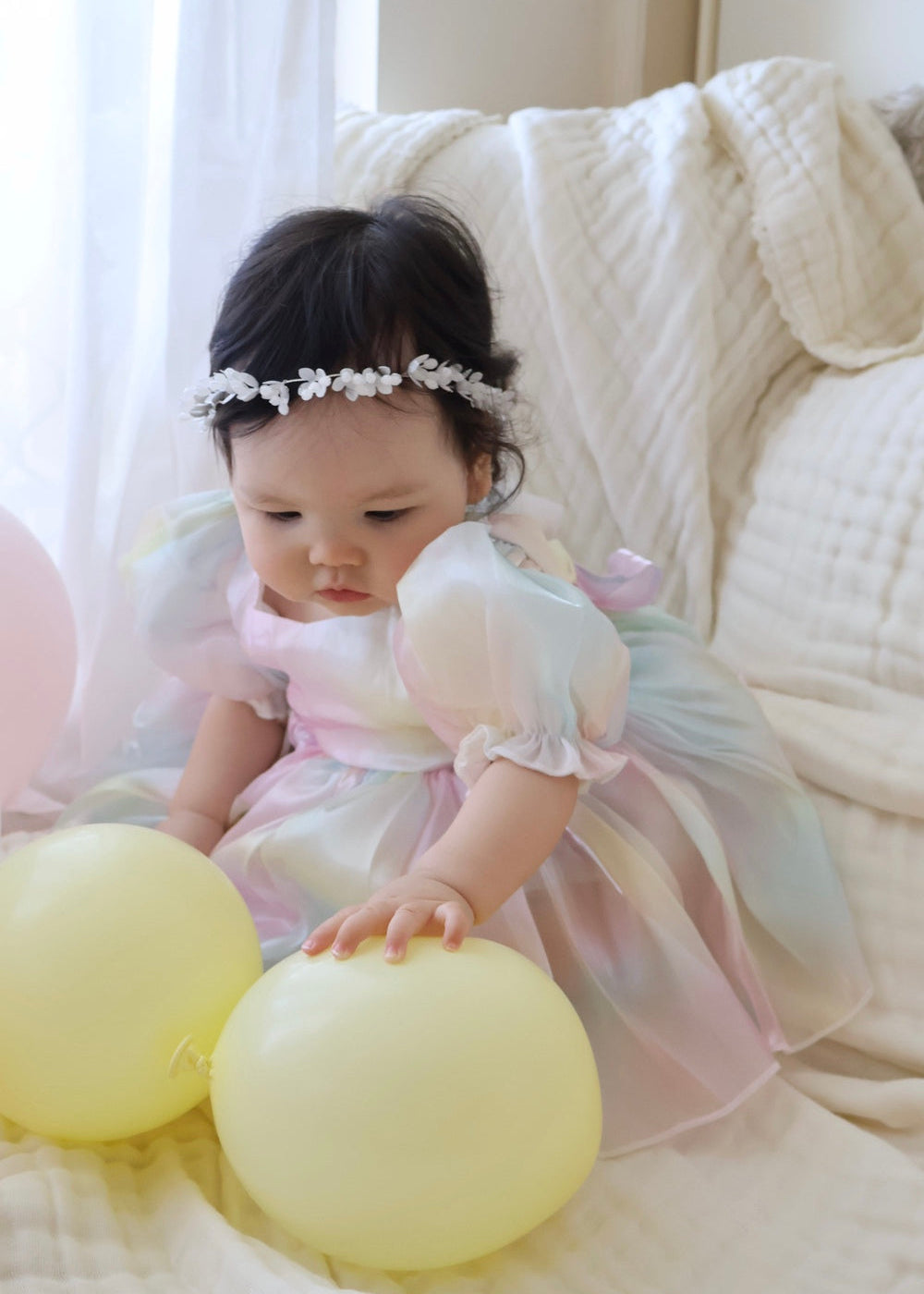 Baby girl in shimmery rainbow organza romper with puff sleeves, smiling at her first birthday