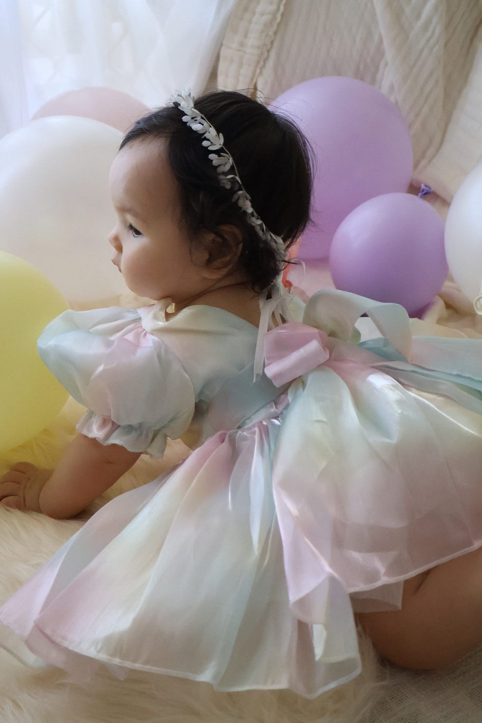 Baby sitting for milestone photos in puff-sleeve rainbow organza romper, true-to-size fit