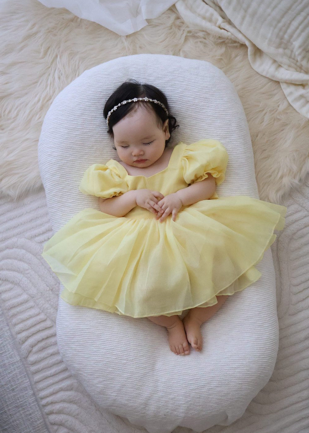 Baby in a yellow dress lying on a white cushion