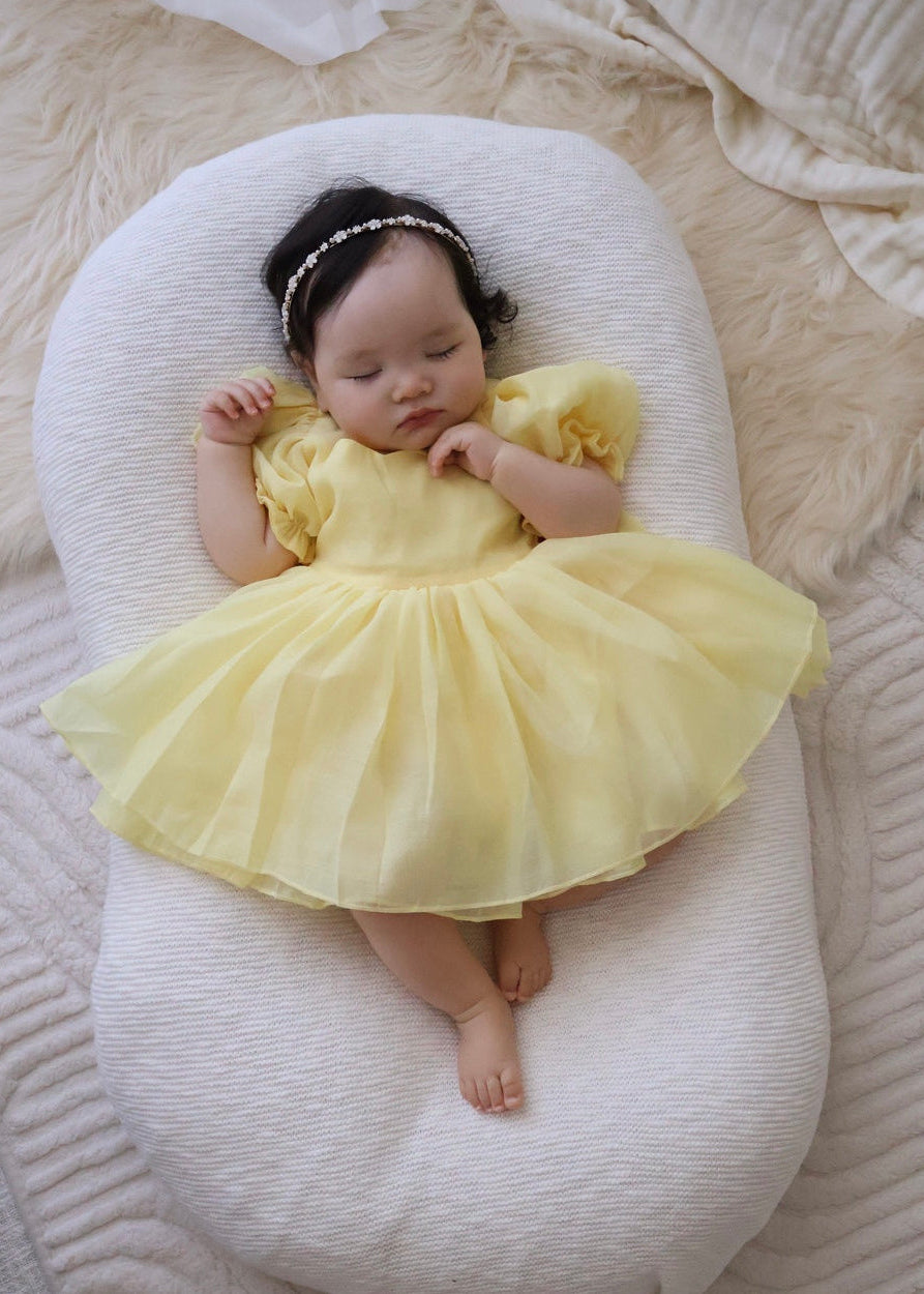 Baby in a yellow dress lying on a white cushion