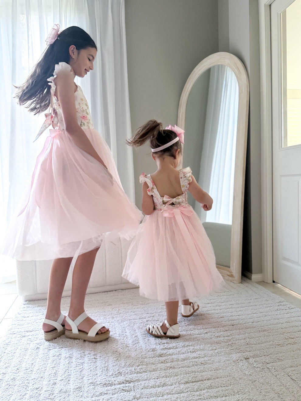 Little girl twirling in light pink Audrey Rose dress with floral print and tulle skirt