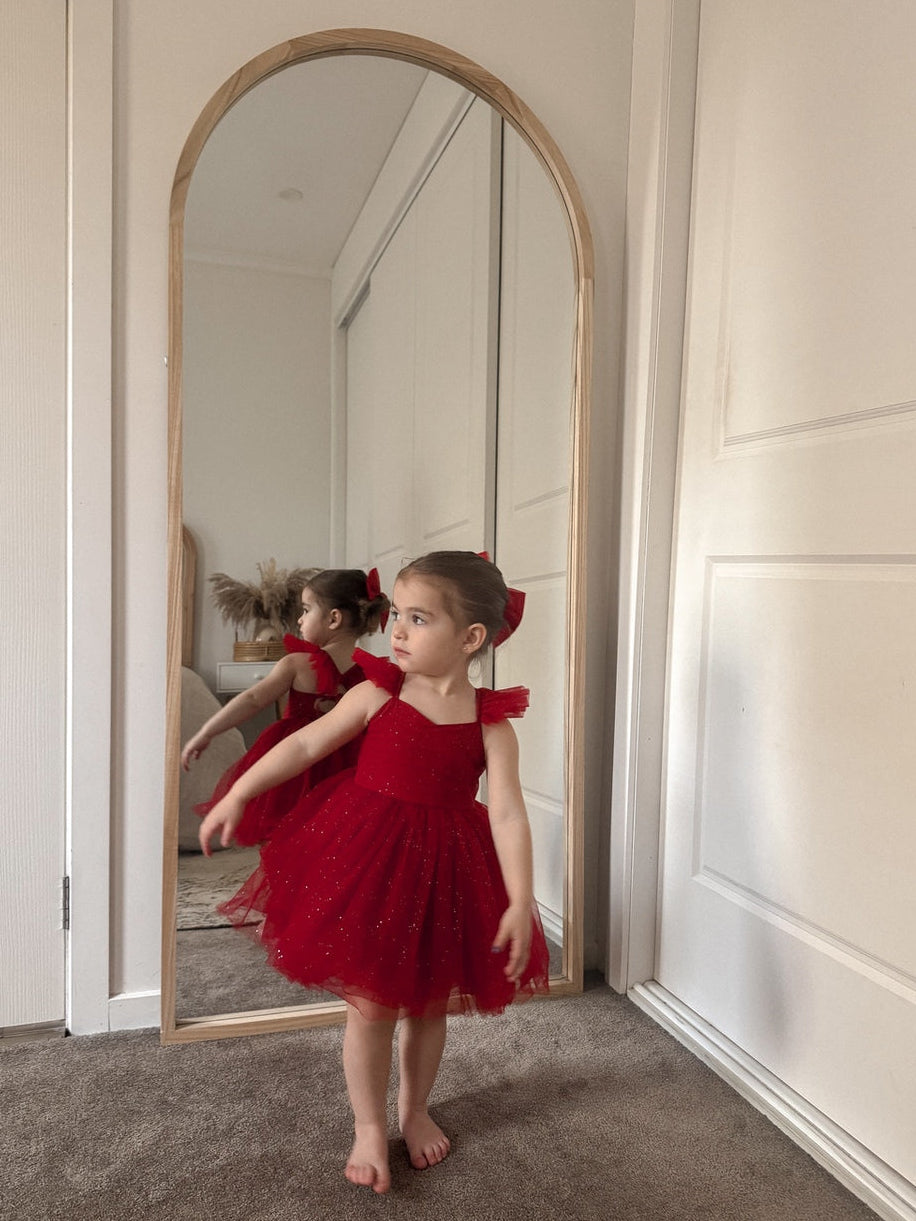 Child in a red dress standing in front of a full-length mirror.