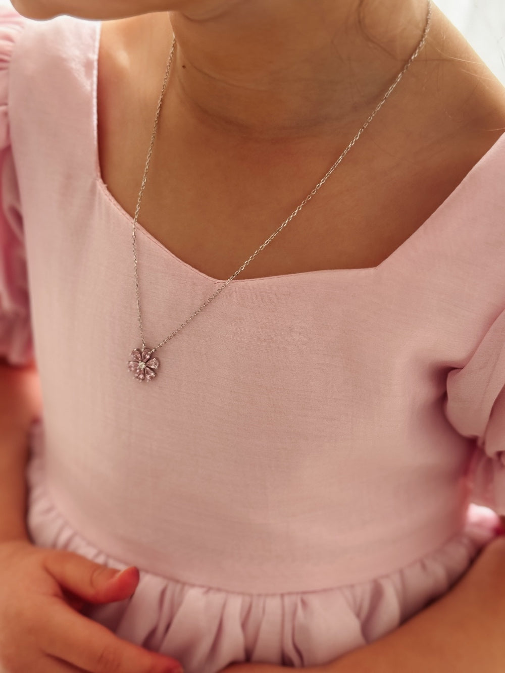 Close-up of silver necklace featuring pink flower charm