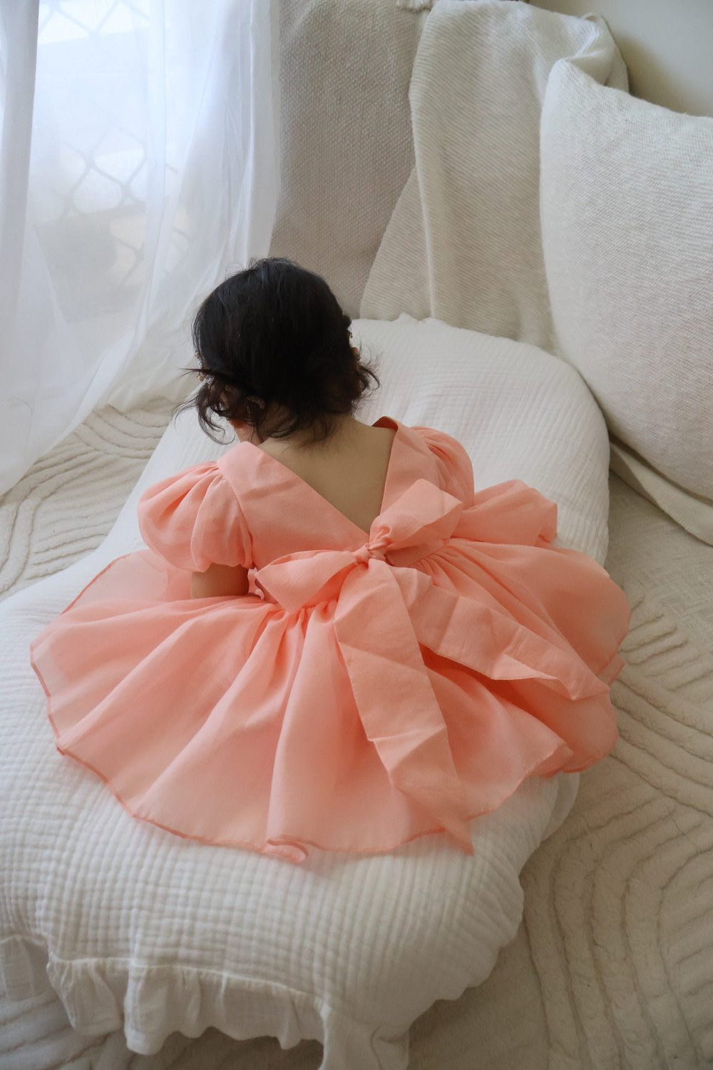 Delia Peach Baby DressBaby girl wearing peach Delia dress with puff sleeves and V-back bow