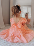 Girls peach party dress with puff sleeves and V-back bow, perfect for flower girls.