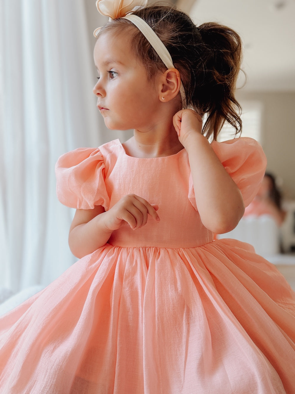 Elegant peach flower girl dress with tulle bow and classic puff sleeves.