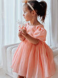 Little girl wearing peach Delia dress with puff sleeves and flowing skirt.