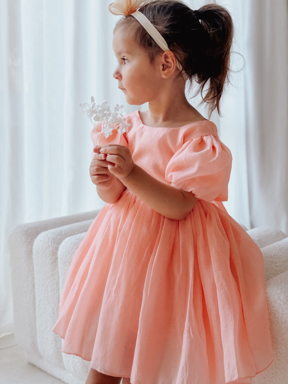 Little girl wearing peach Delia dress with puff sleeves and flowing skirt.