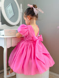 Girl wearing a hot pink puff-sleeve dress with V-back and bow – Delia Girls Hot Pink Dress