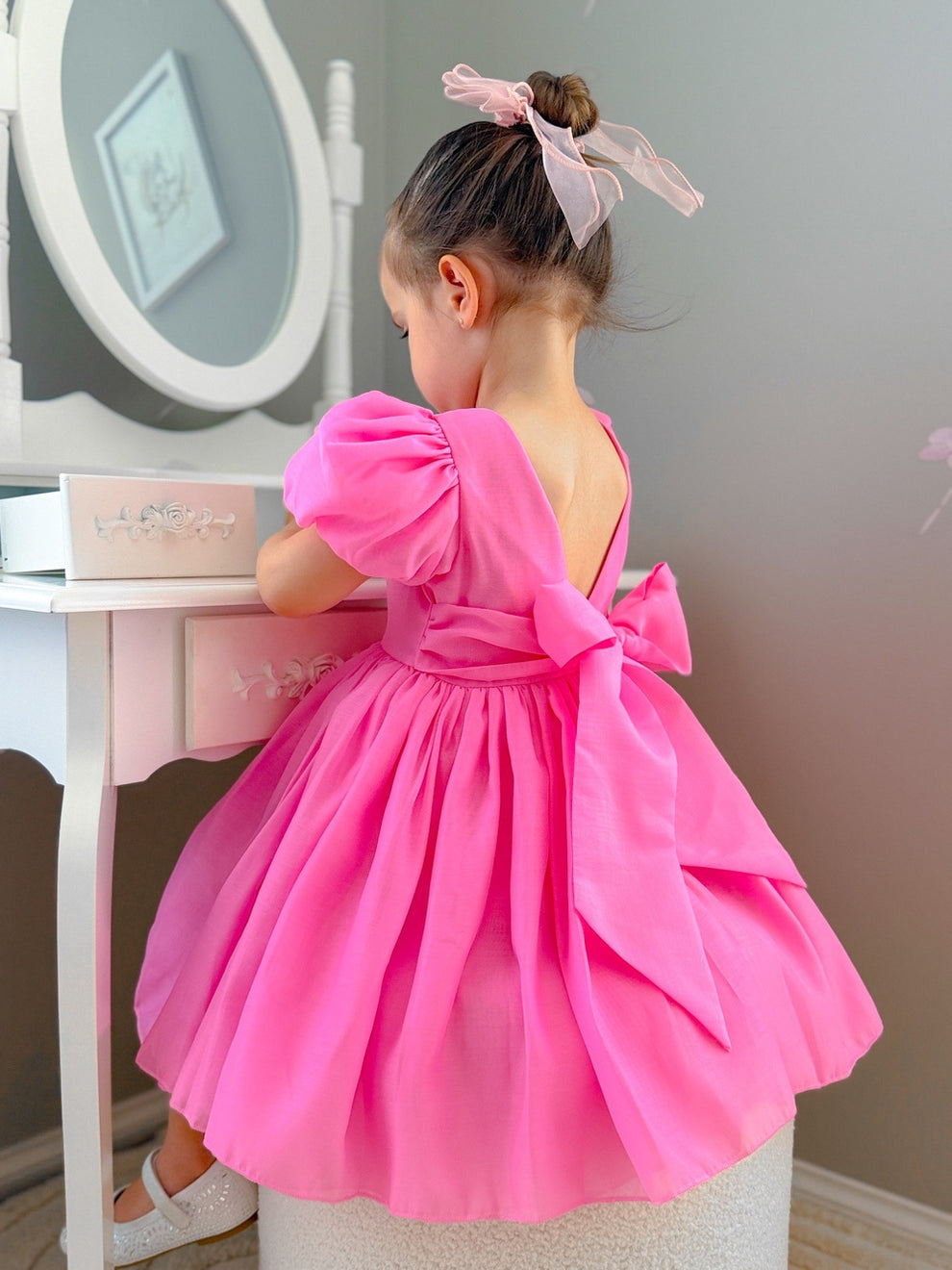 Girl wearing a hot pink puff-sleeve dress with V-back and bow – Delia Girls Hot Pink Dress
