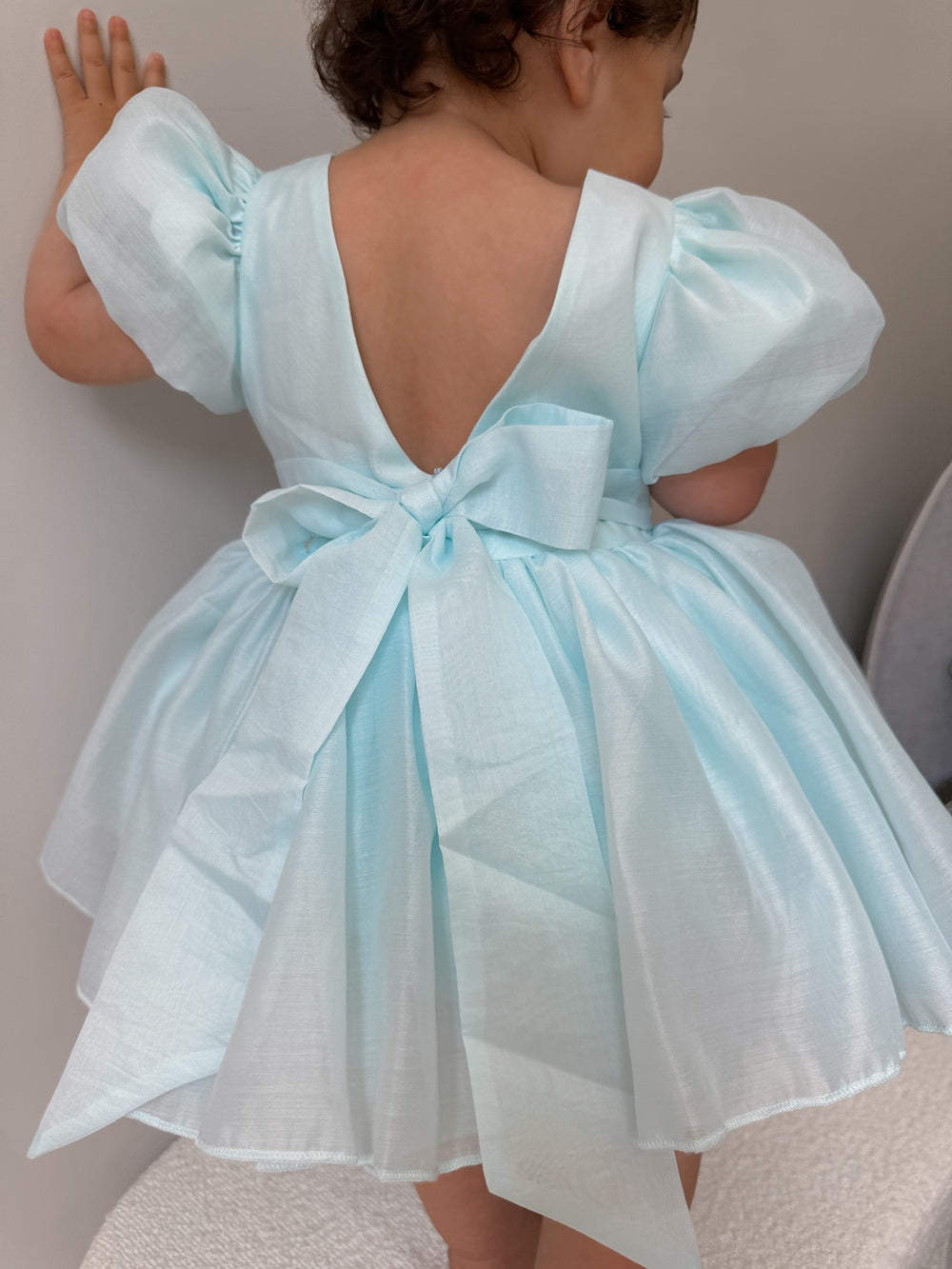 Baby girl wearing pale blue Delia dress with statement back bow
