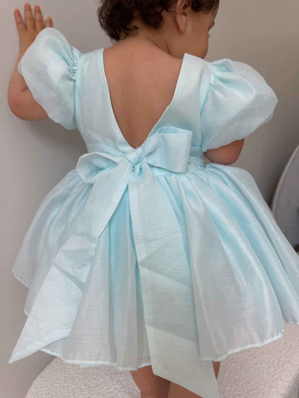 Baby girl wearing pale blue Delia dress with statement back bow