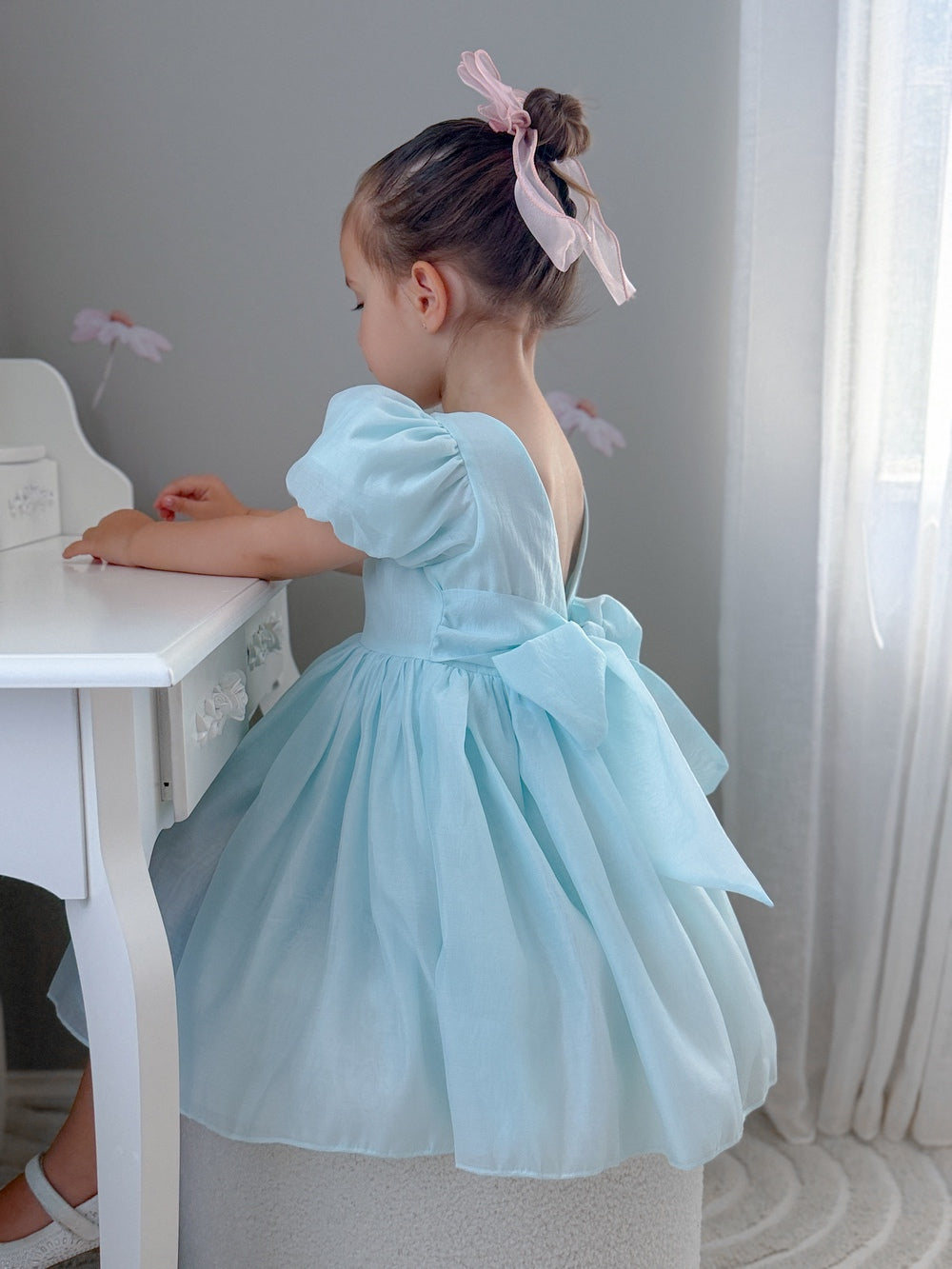Delia Girls Pale Blue Dress - Shop AllGirl wearing a pale blue flower girl dress with puff sleeves and a bow at the back