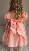 Back view of Delia Girls Peach Dress featuring statement bow and V-back design