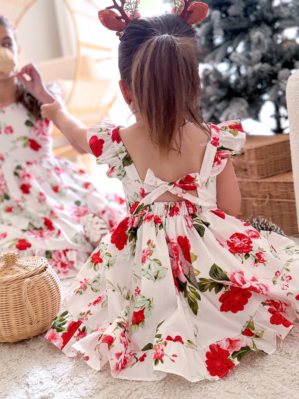 Faith Girls Christmas Rose Dress - Christmas Dresses and RompersSisters in matching Christmas floral dresses playing near presents and christmas tree