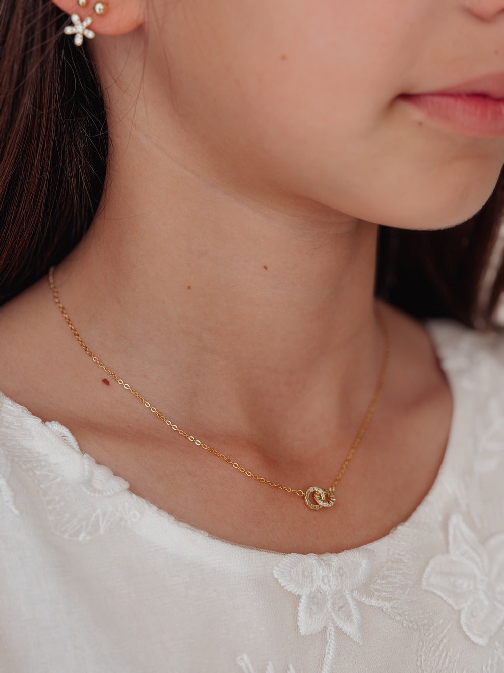 Young girl wearing gold linked necklace with white outfit