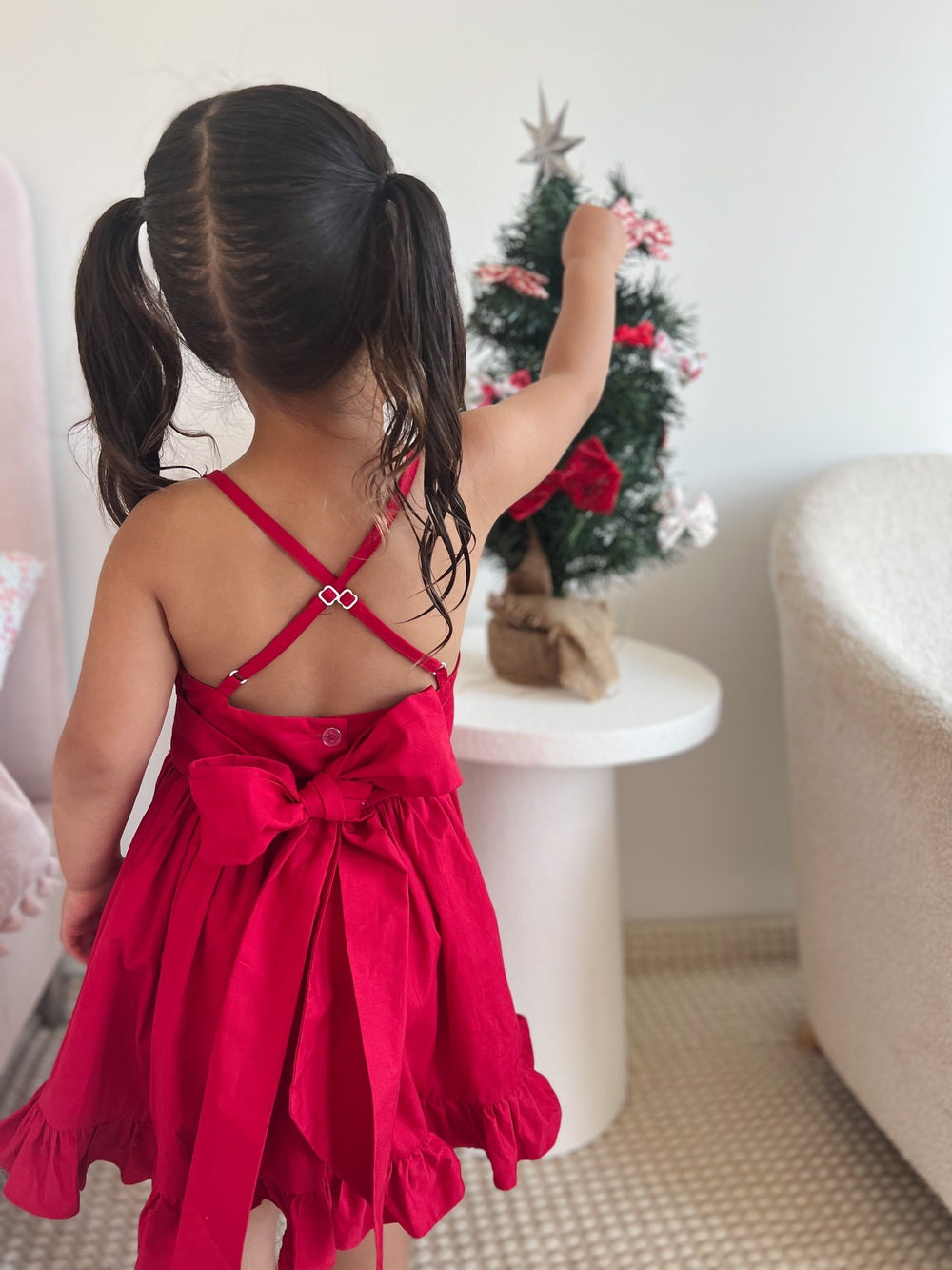 Girl wearing red cotton Christmas dress with large bow posing for Santa photos
