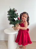 Little girl holding mini Christmas tree in red cotton Christmas dress for family holiday photos