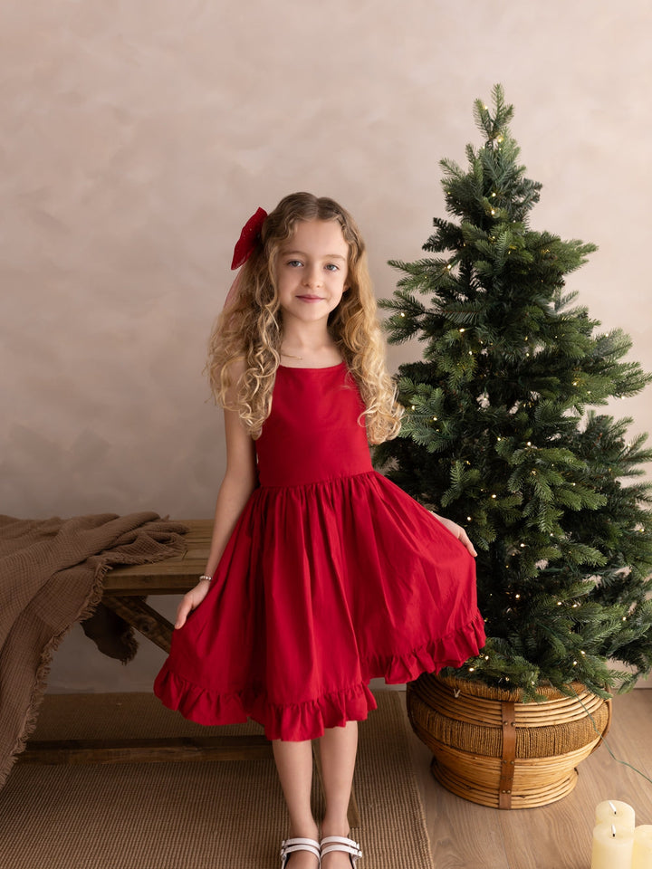 Front view of a girl wearing the Holly red Christmas dress, holding out the full skirt with ruffle hem