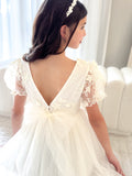 Back view showing V-shaped back and delicate pearl button detail on ivory dress