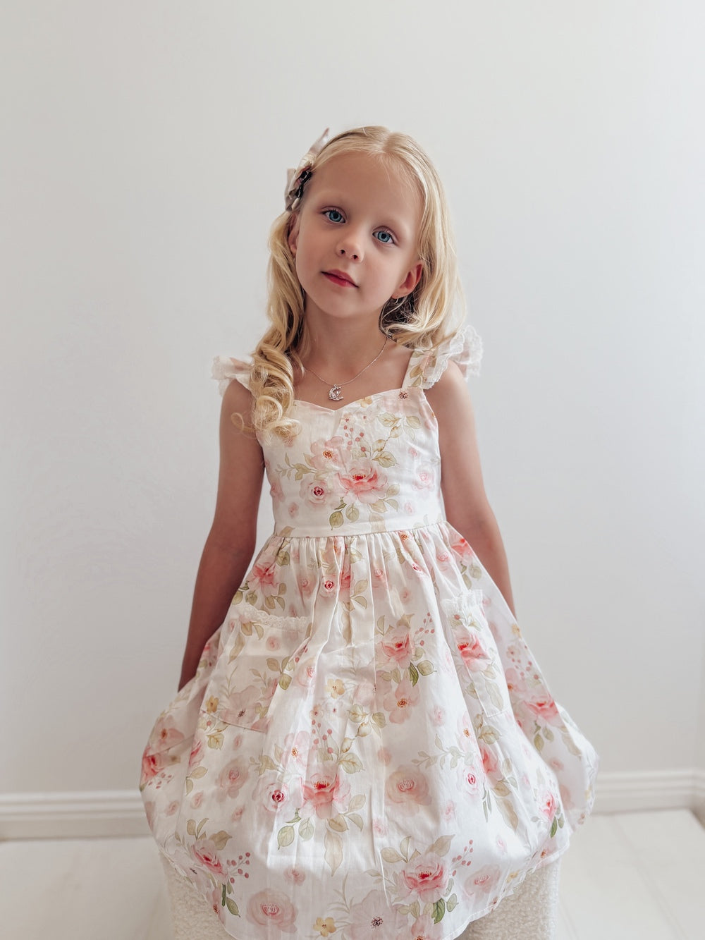 Lucinda Girls Floral Dress - New ArrivalsLittle girl wearing Lucinda Floral Dress with bow back and lace pockets