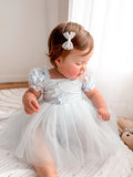 Lila dusty blue baby occasion dress with tulle skirt, seated view.