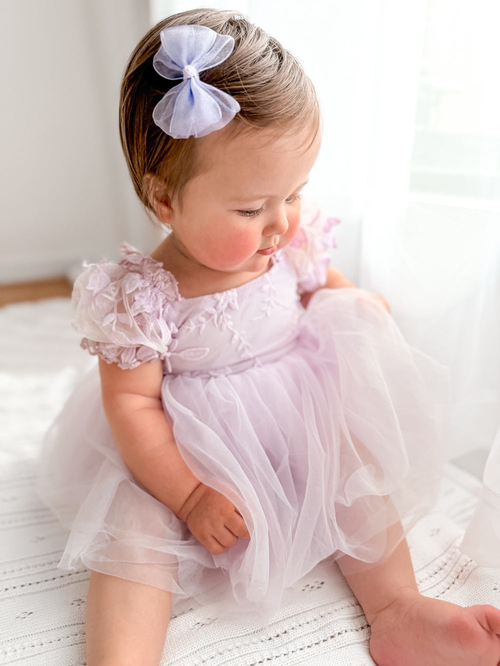 Baby girl wearing lilac embroidered dress with matching hair bow