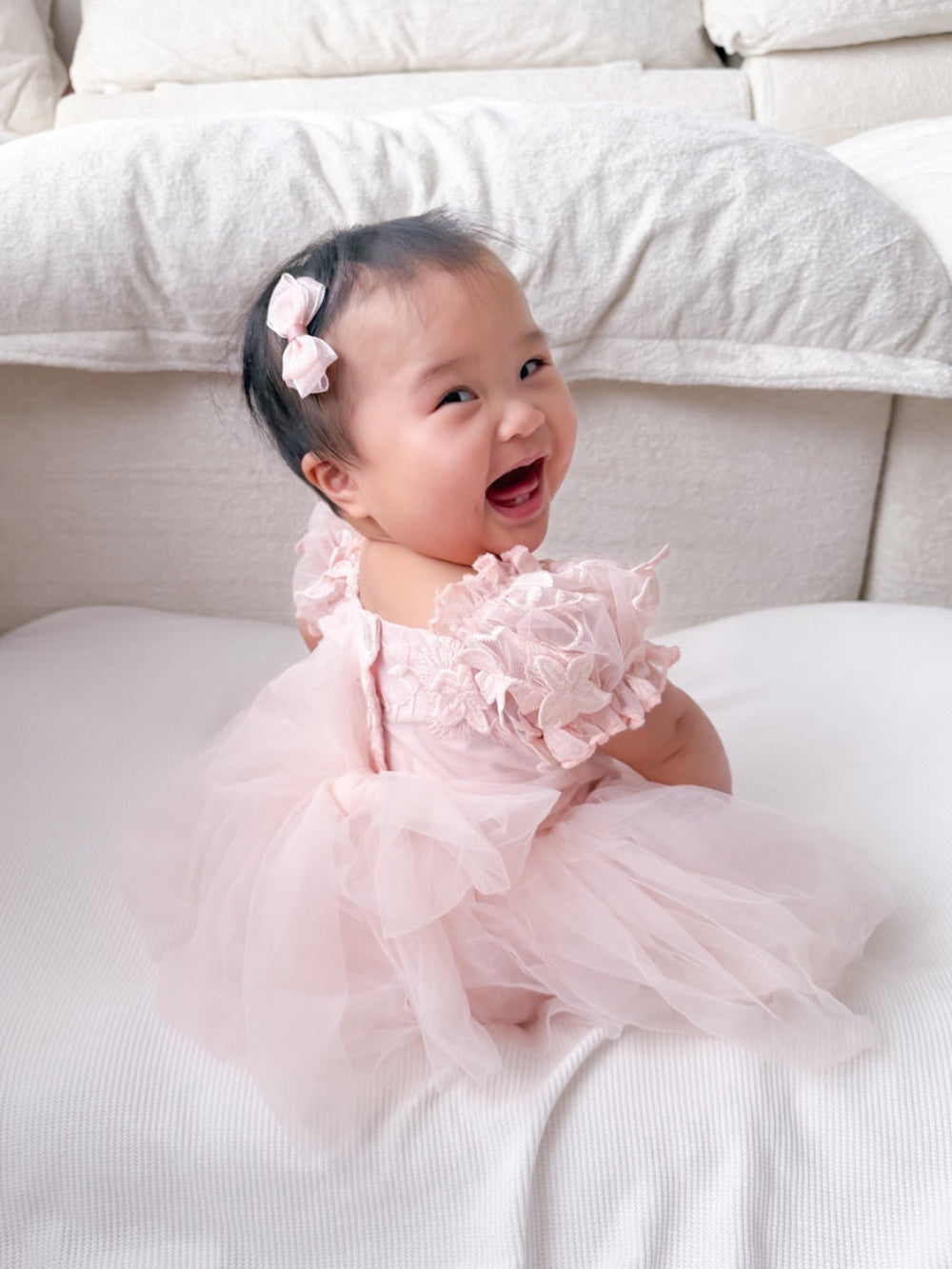 Lila soft pink embroidered baby dress with floral puff sleeves, three-quarter view.
