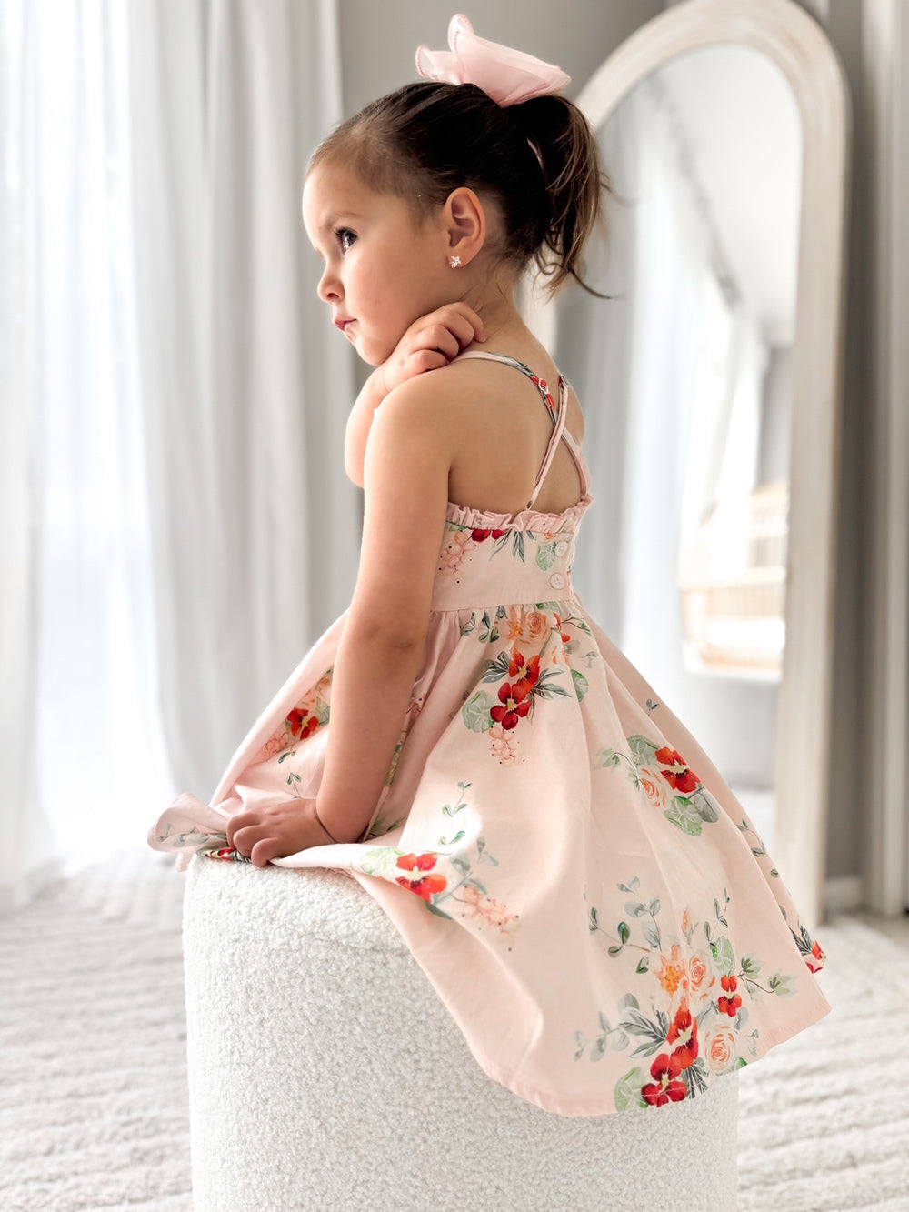 Side angle of the Marley Girls Christmas Dress highlighting the light pink cotton fabric with red floral pattern and breezy above-knee length fit.
