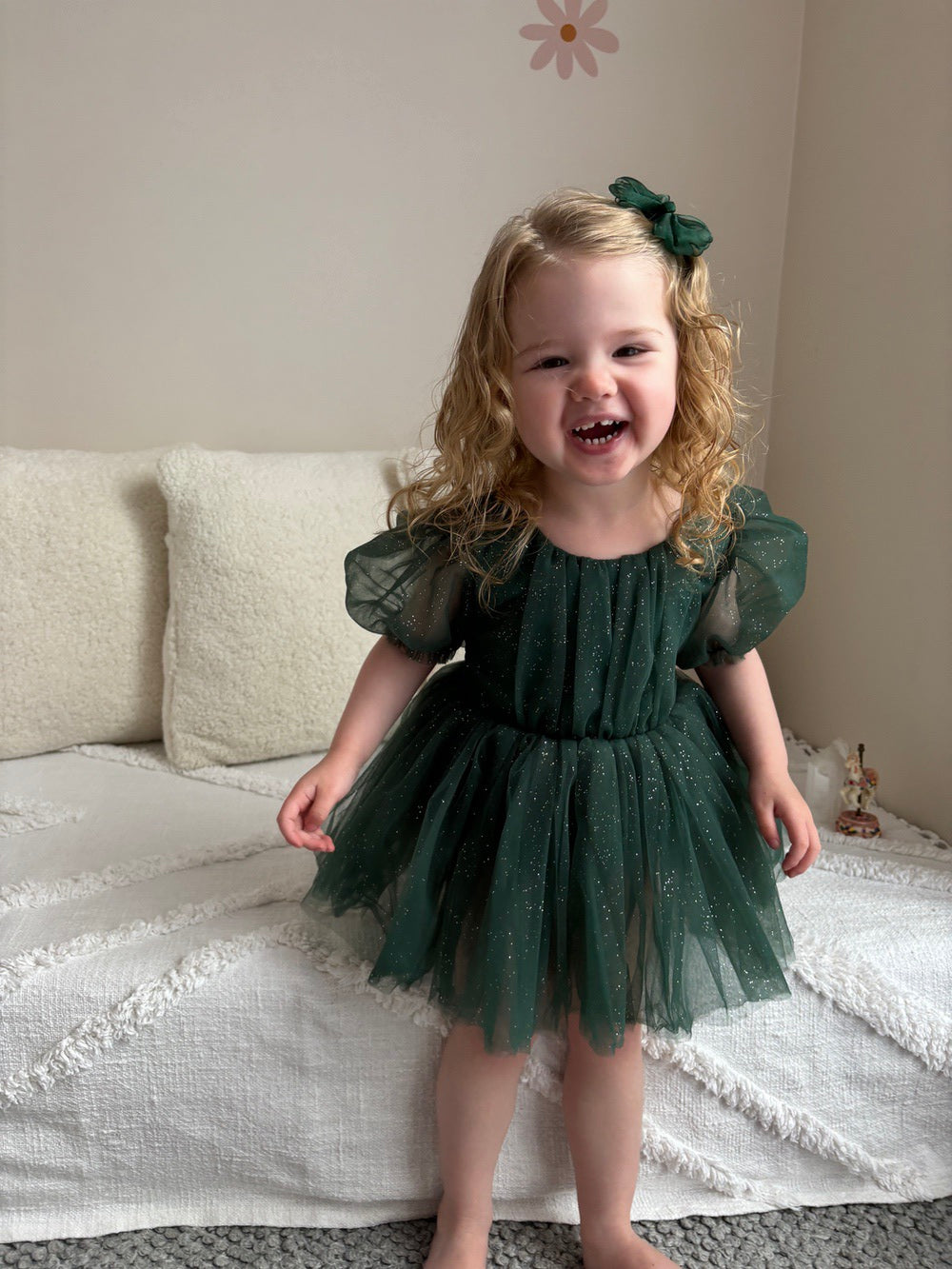 Toddler smiling in sparkly green Christmas romper during holiday photoshoot
