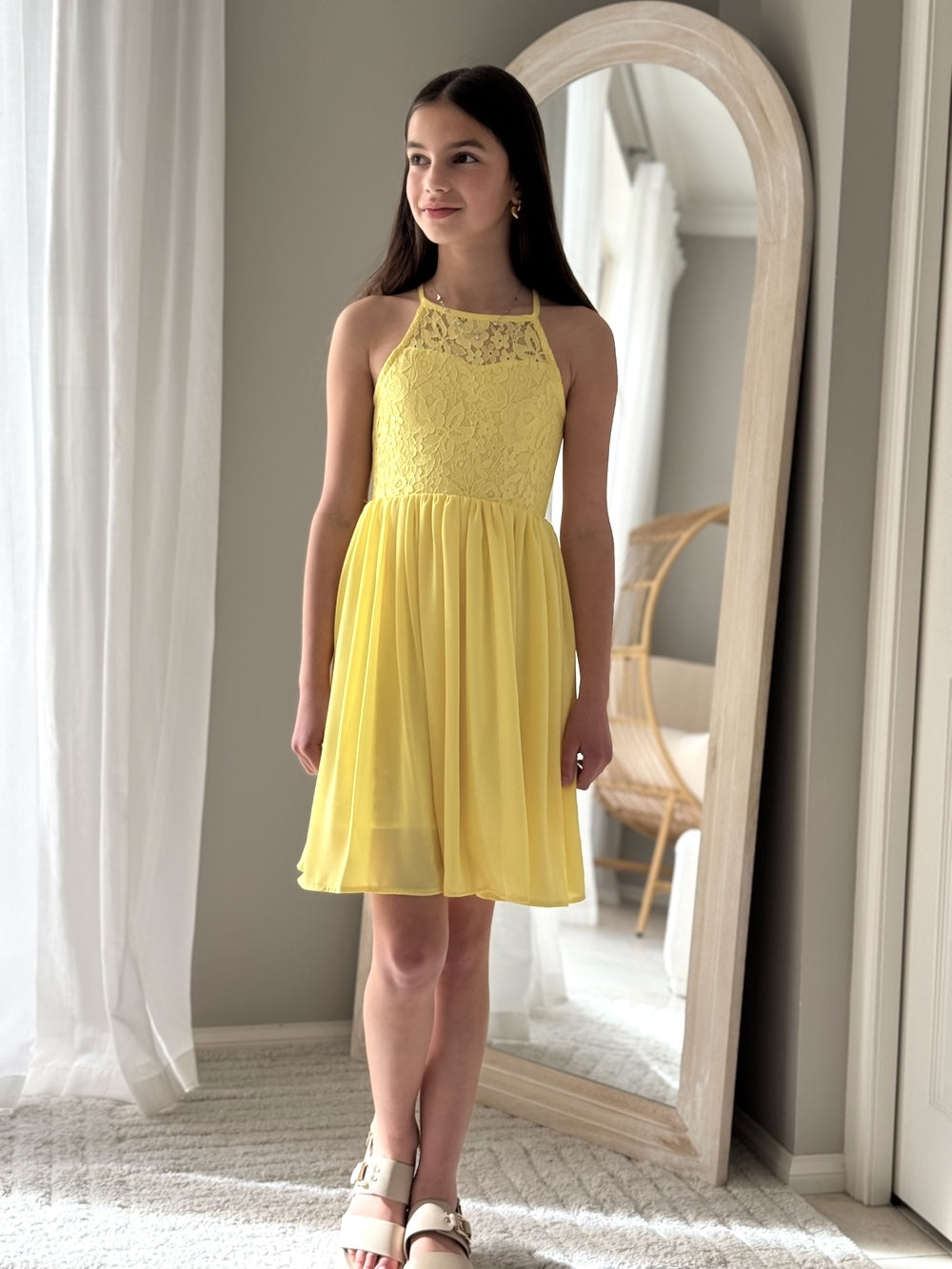 Tween girl in a yellow graduation dress standing in front of a mirror.