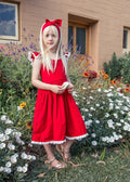Girl wearing the Rosie red Christmas dress with white broderie trim in a flower garden