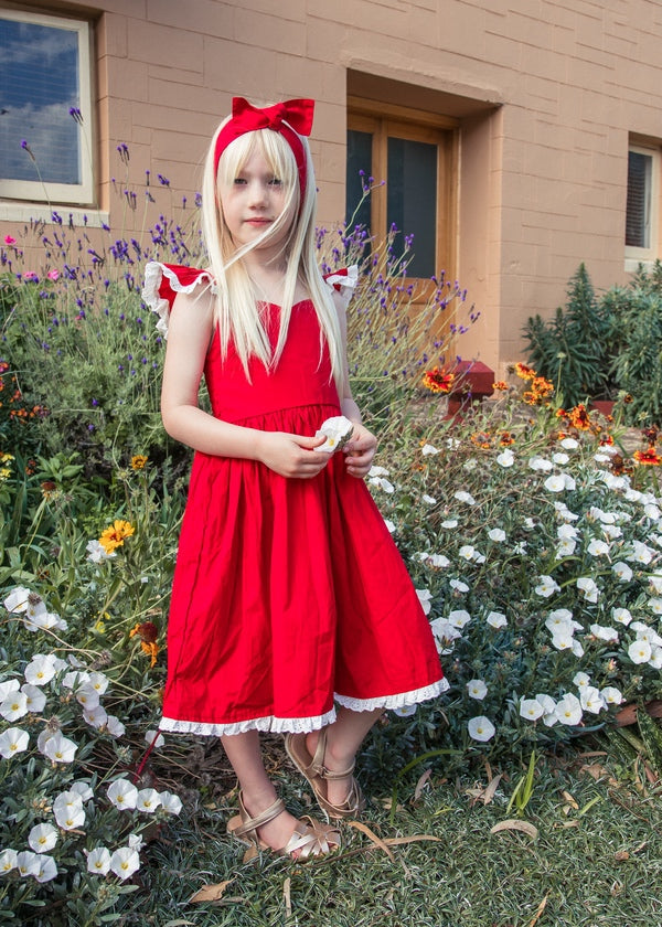 Girl wearing the Rosie red Christmas dress with white broderie trim in a flower garden