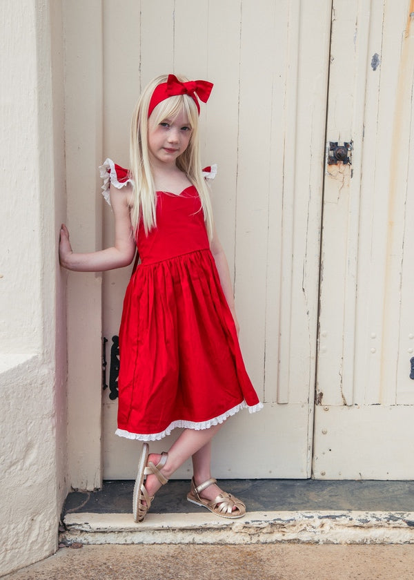 Girl modelling the Rosie red Christmas dress and matching head wrap in a doorway
