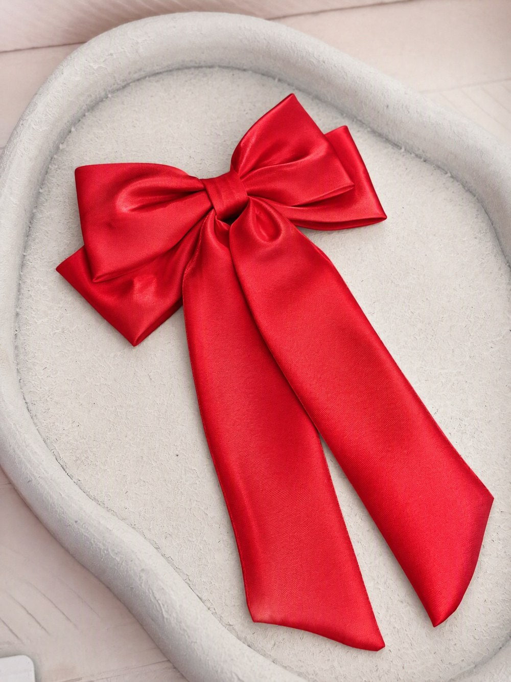 Amelie red satin hair bow with double loops and long tails, shown on a cream chair.