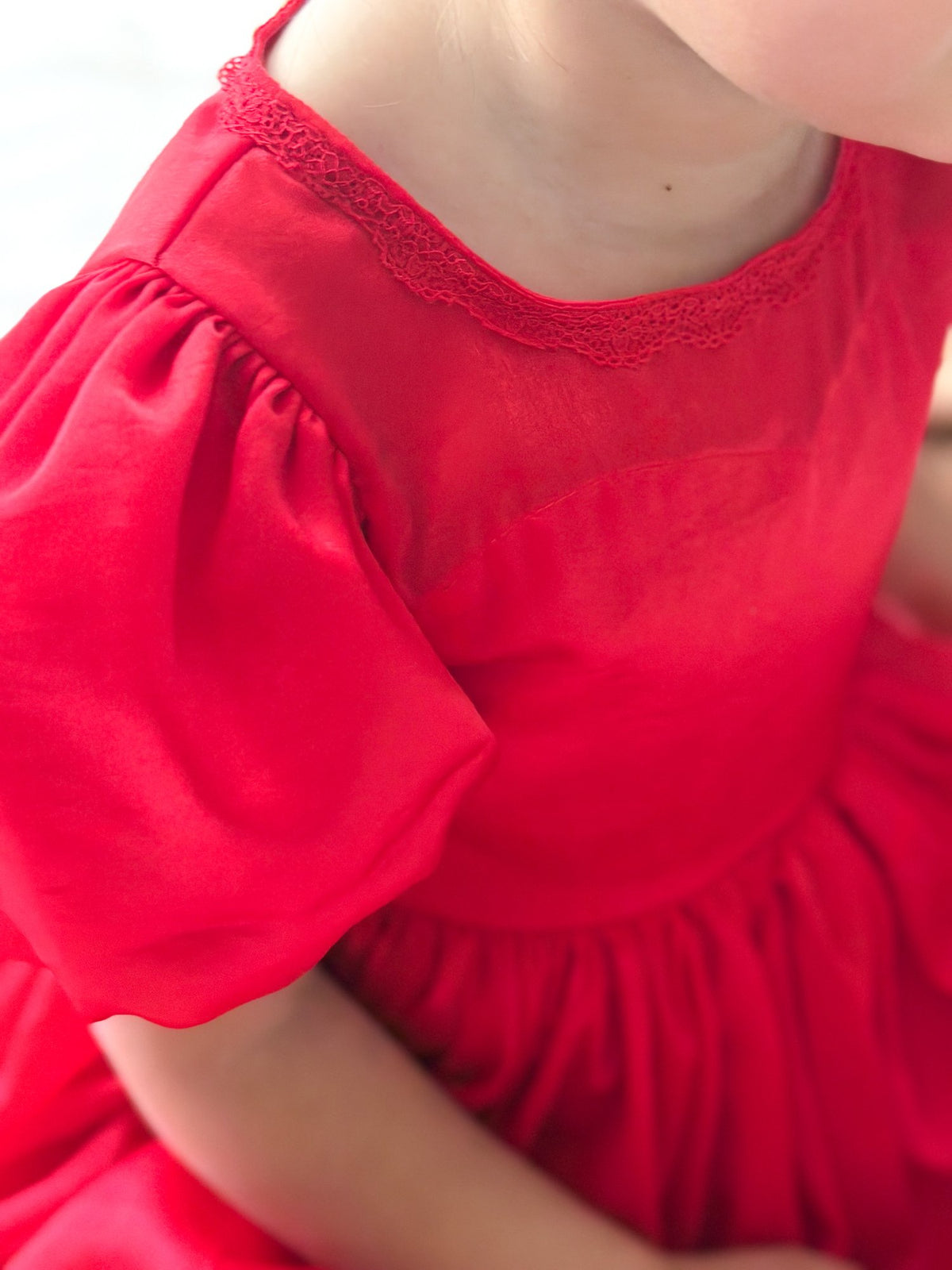 Close-up of the Evangeline red Christmas dress showing the lace-trimmed neckline, shimmering fabric and puff sleeve.