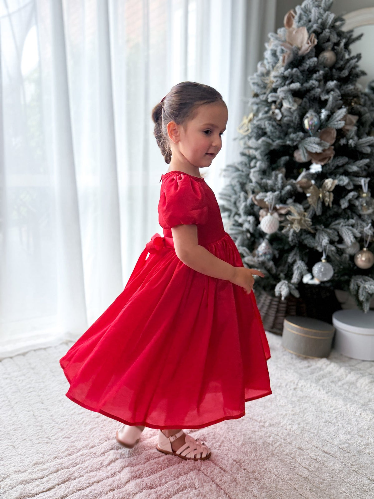 Side view of the Evangeline girls red Christmas dress showing the gathered skirt in movement beside a Christmas tree.