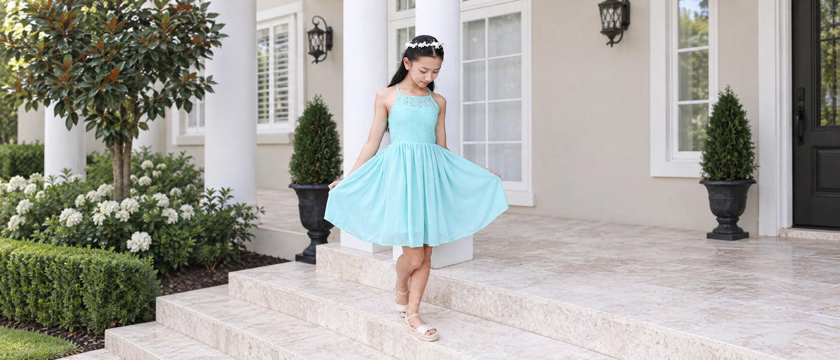 Norah turquoise occasion dress with floral lace, photographed on a cream veranda