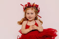 Front view of the Winterberry red flower crown and trailing red ribbons on a seated girl